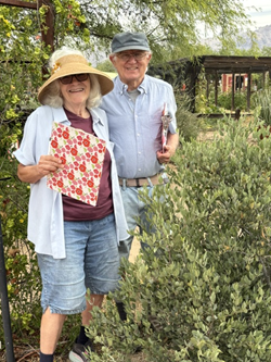 Rita and Steve stand next to a jojoba bush holding clipboards for data collection